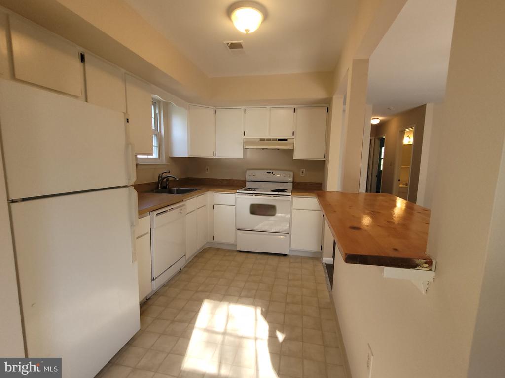 Kitchen with white cabinets and appliances, a window over the sink, and a long wooden breakfast bar.