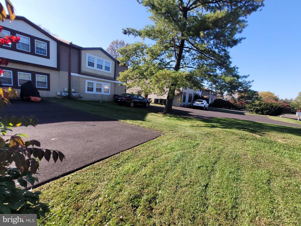 Multi-unit building beside a large pine tree, with a lawn and paved parking area.
