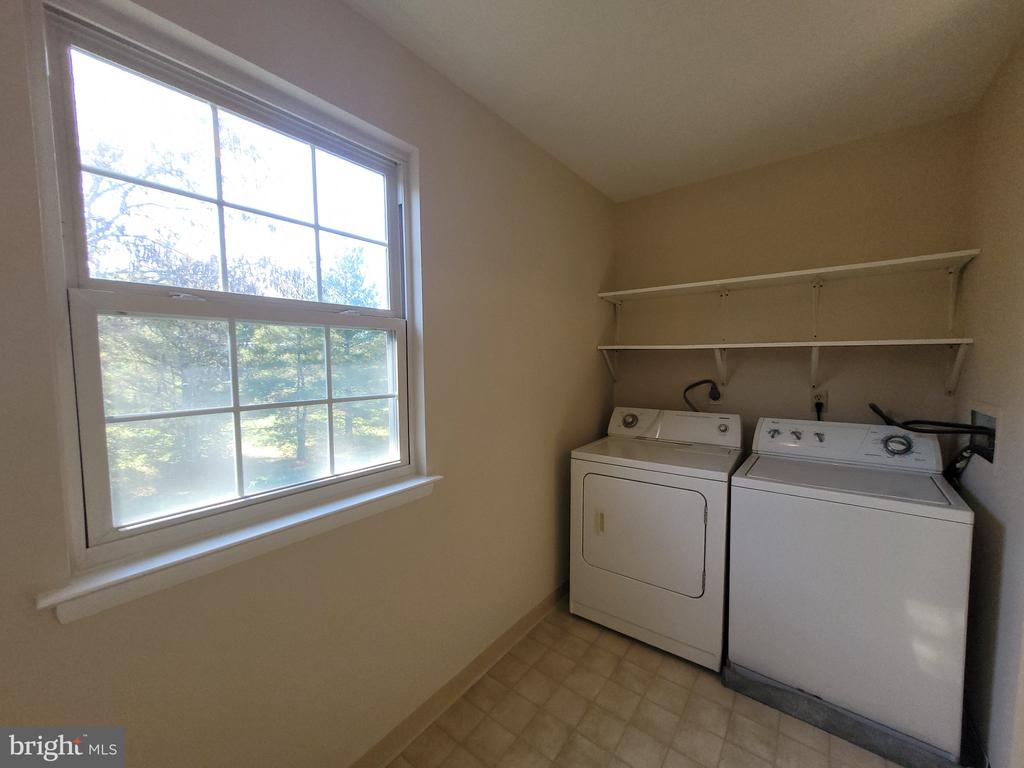 Laundry room with a washer and dryer beneath shelves beside a large window.