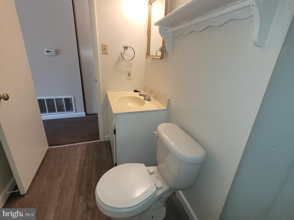 Bathroom with a white toilet, compact vanity, and wall-mounted shelf.