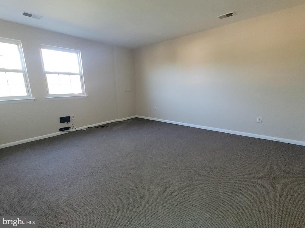 Empty carpeted room with two windows and neutral walls.