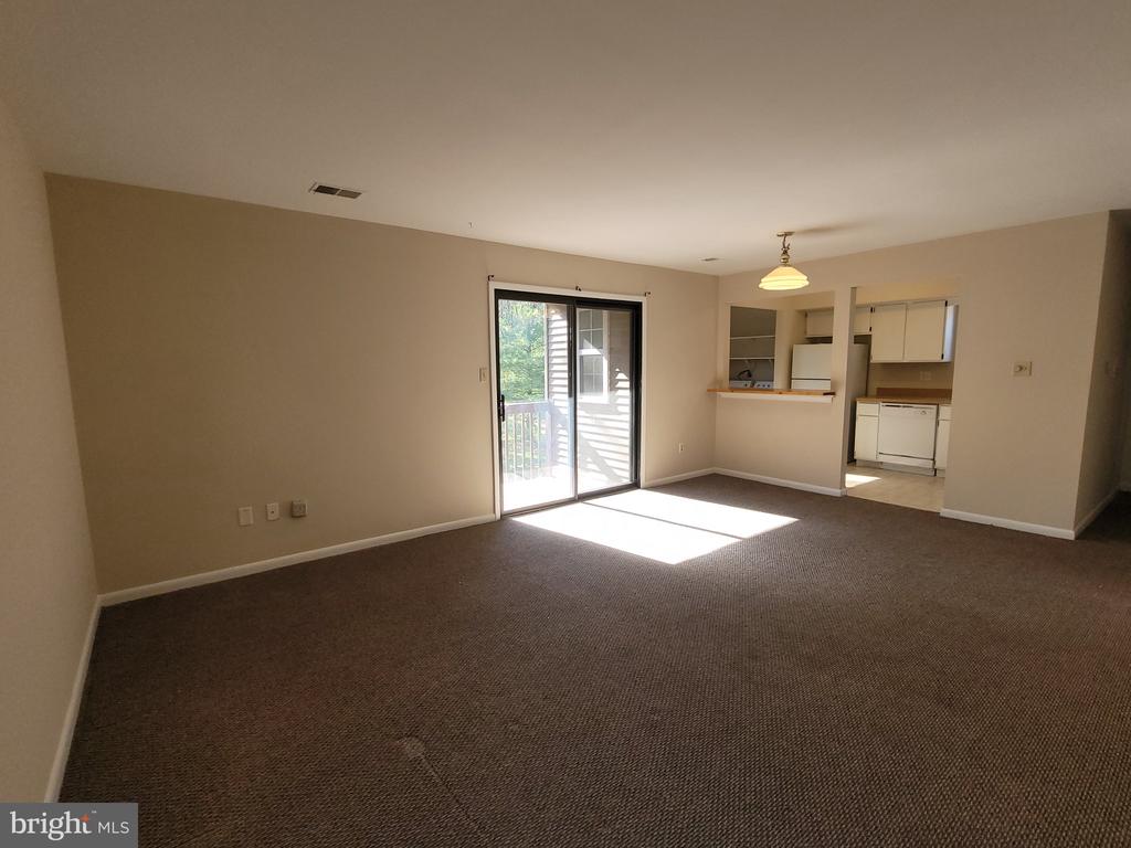 Empty carpeted living room with a sliding glass door and adjoining kitchen.