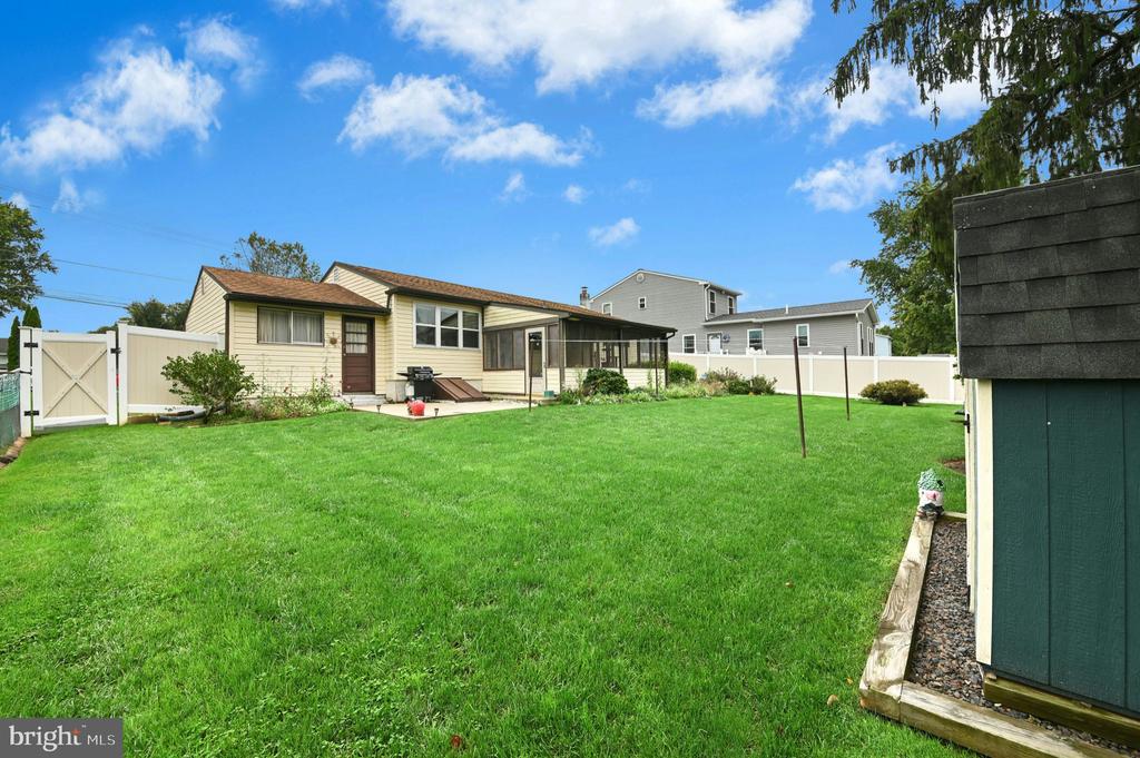 Backyard with a broad lawn, white privacy fence, and beige house with a screened porch.