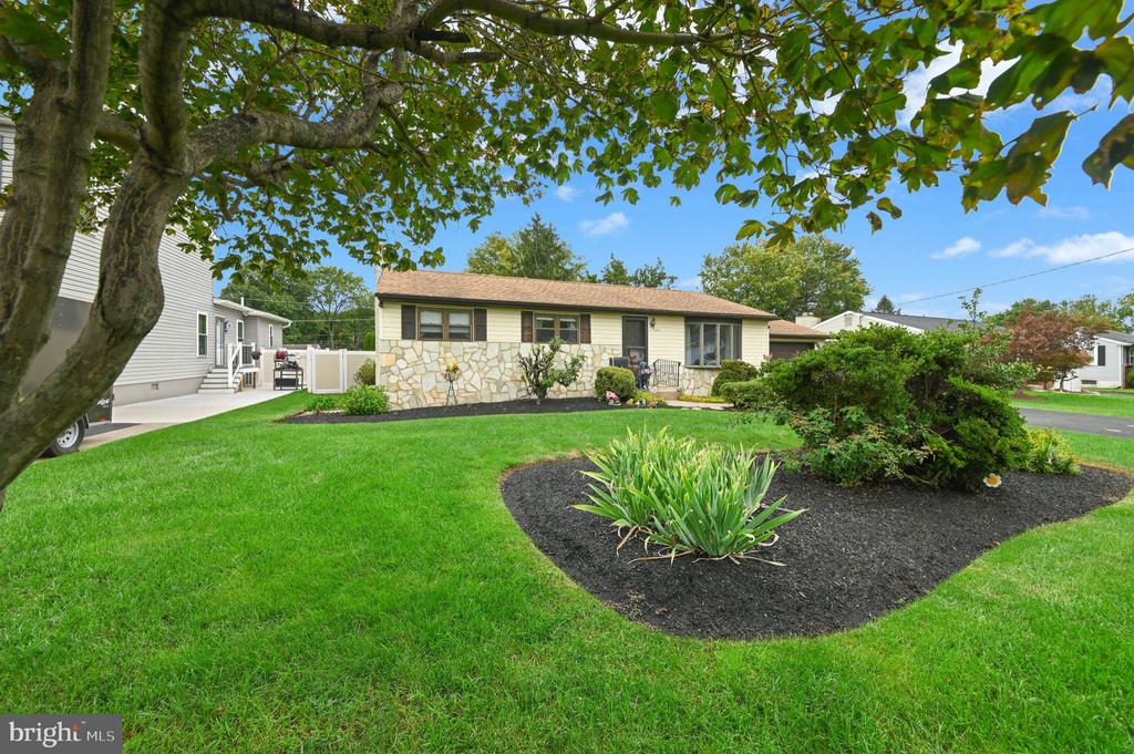 Single-story ranch home with a stone facade, landscaped garden, and mature trees.