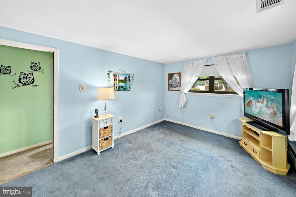 Blue-carpeted room with pale blue walls, a curtained window, and a television on a wood console.