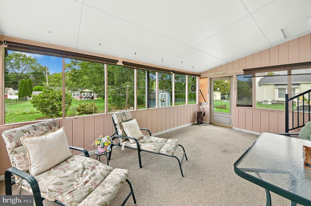 Enclosed porch with cushioned seating and large windows overlooking a green yard.