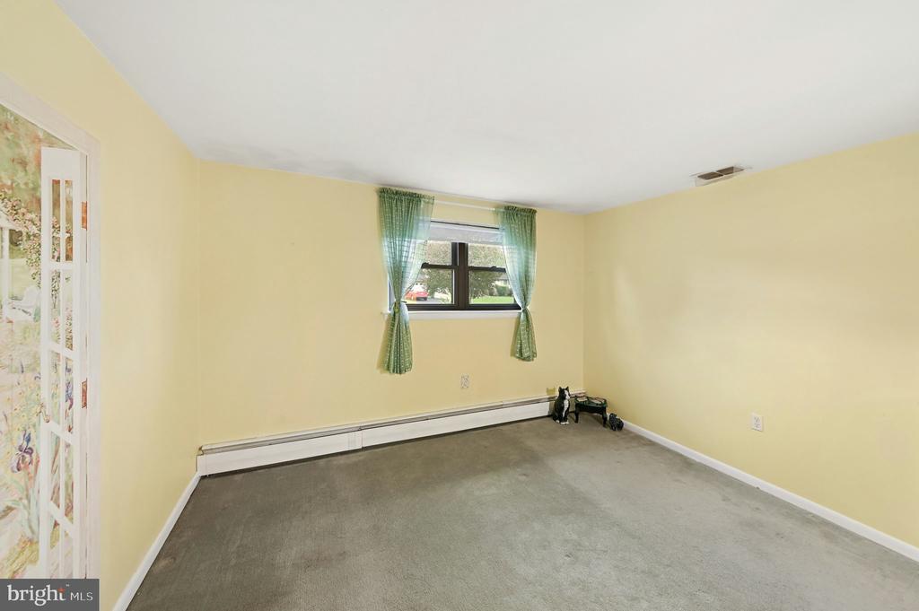 Mostly empty room with yellow walls, gray carpet, green window curtains, and a baseboard heater.