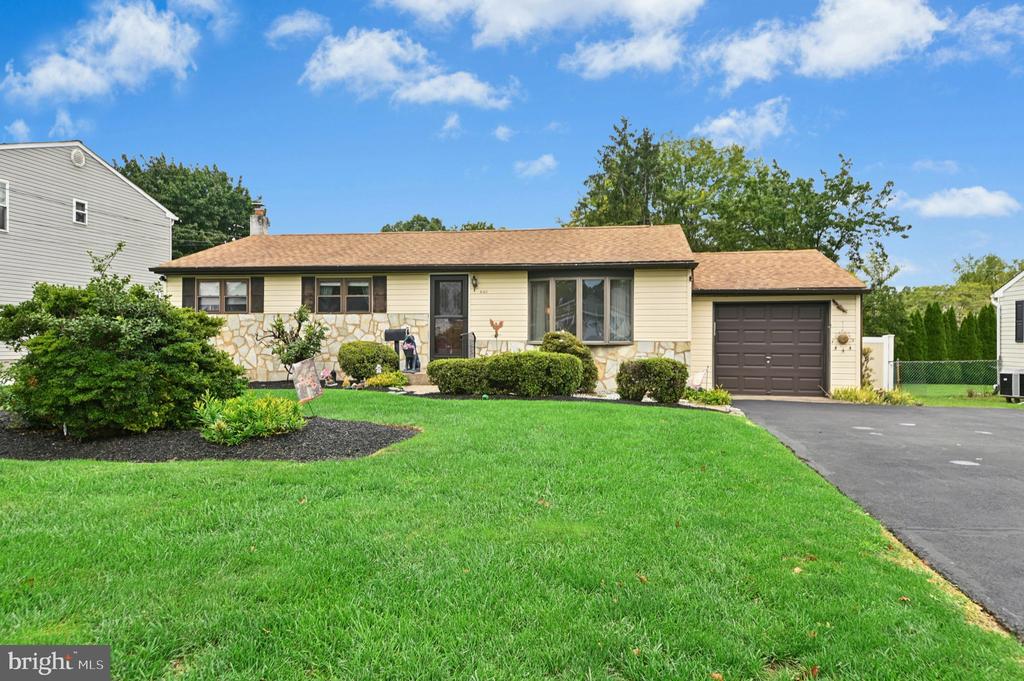 Single-story beige house with a stone-accented facade, attached garage, and broad green lawn.