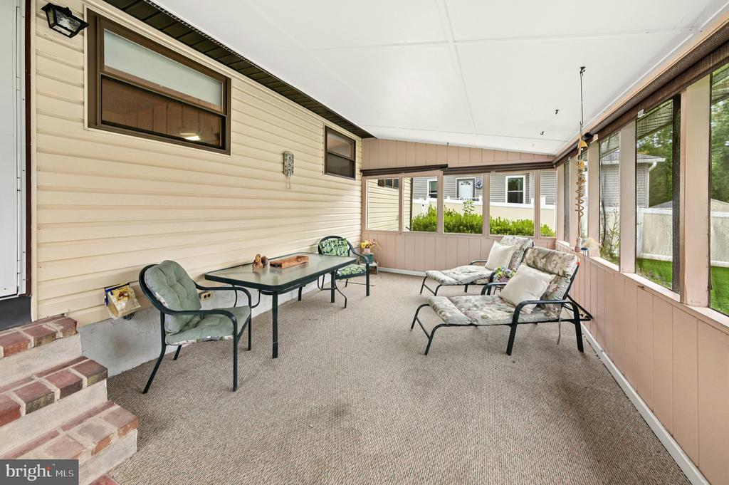 Furnished enclosed porch with screened windows, carpet, a table, and lounge chairs.