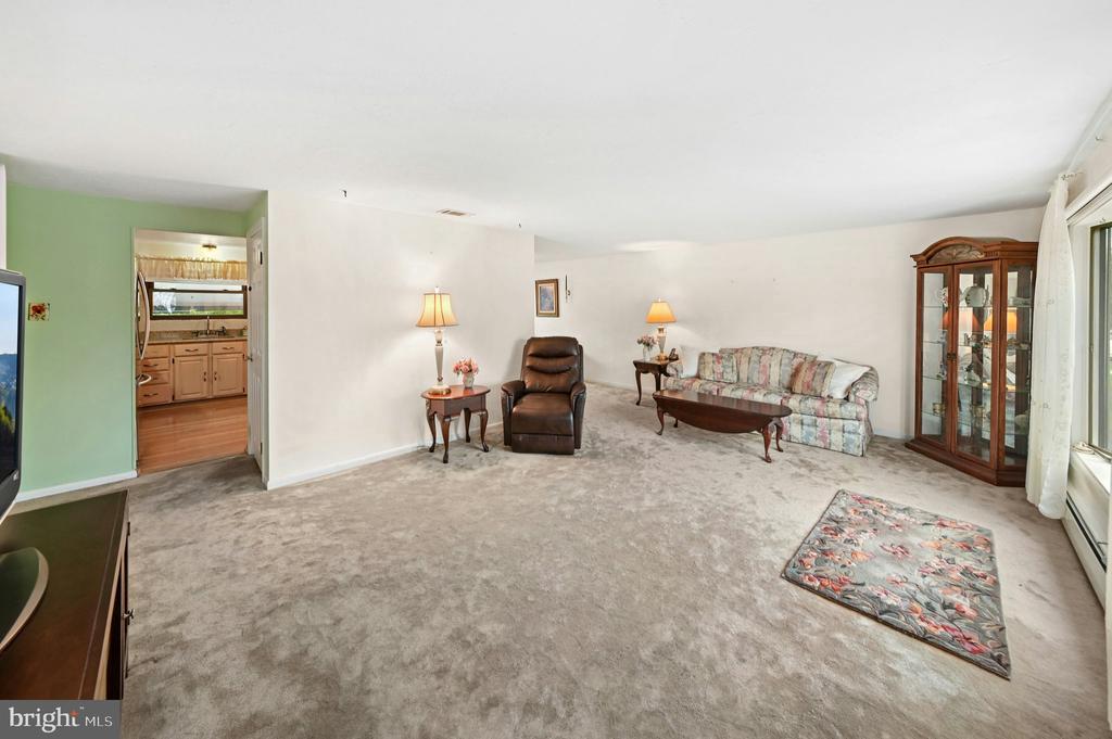 Living room with floral sofa, leather recliner, beige carpet, and a glass-front display cabinet.