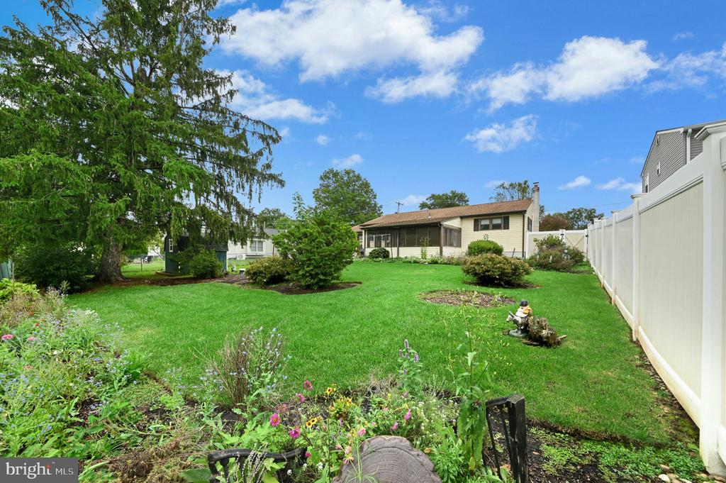 Home's backyard with a broad lawn, flower beds, mature evergreen, and white privacy fence.