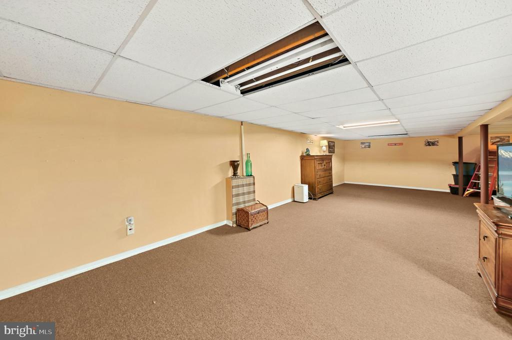 Carpeted basement room with tan walls, wooden furniture, and an exposed ceiling light fixture.