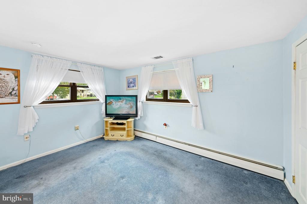 Light blue room with blue carpet, two curtained windows, and a television on a small stand.