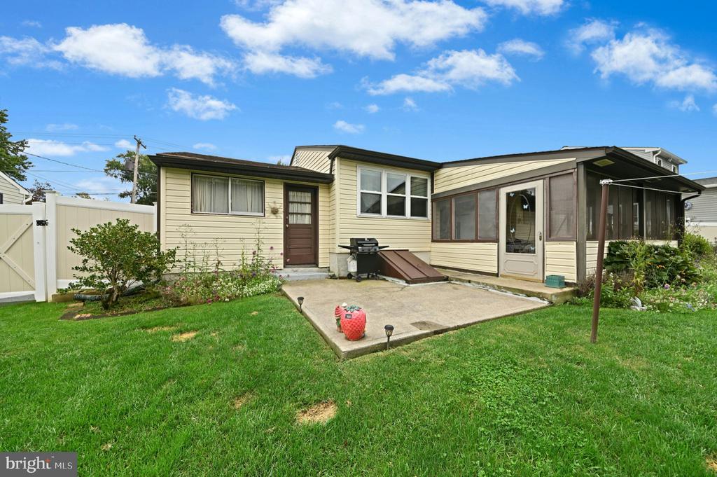 Rear of a beige single-story home with a screened porch, concrete patio, and fenced lawn.
