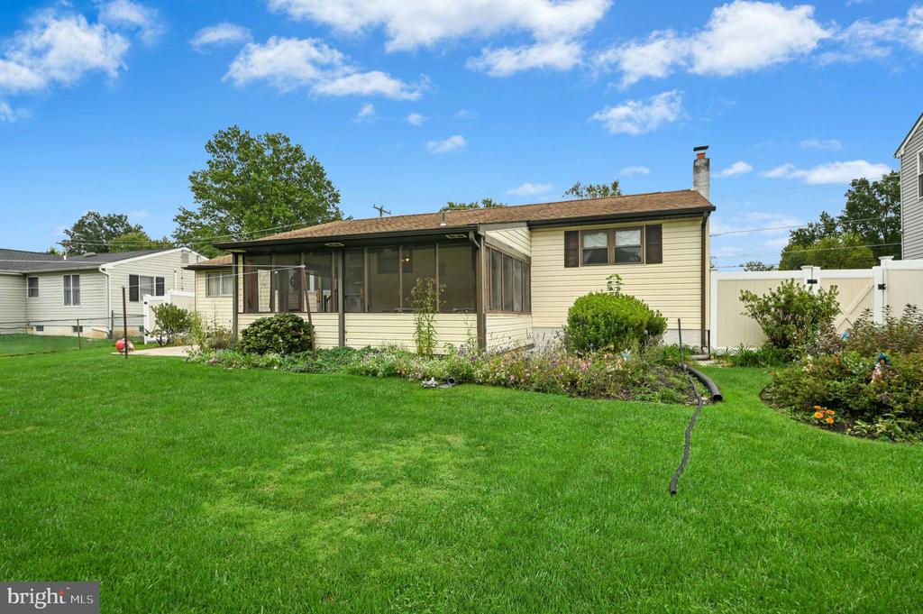 Rear of a pale yellow house with a screened porch, garden beds, and a broad lawn.