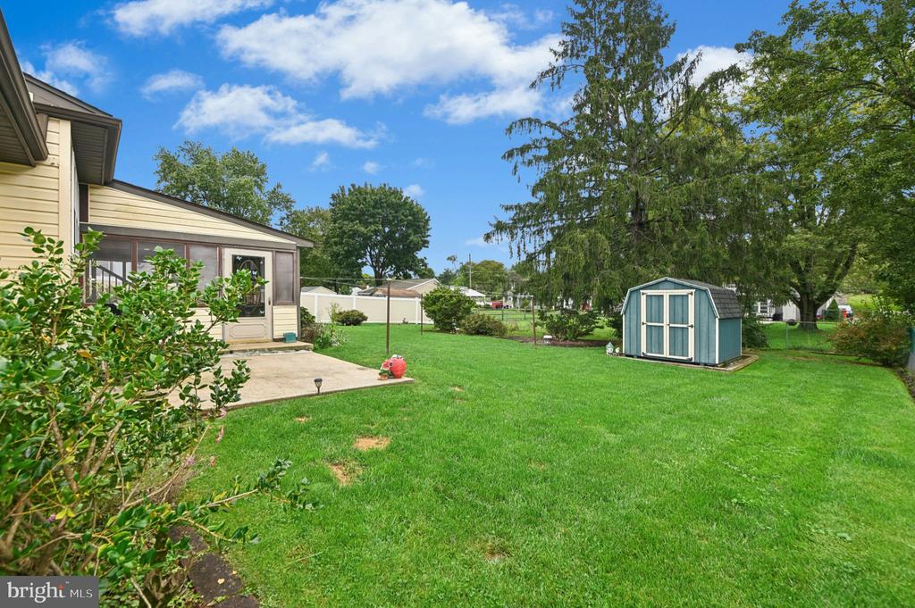 Backyard with a broad green lawn, blue storage shed, mature trees, and covered patio beside the house.