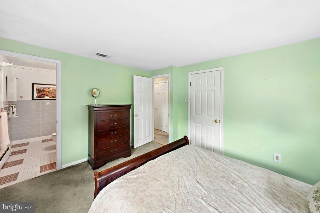 Bedroom with pale green walls, a dark wood dresser, and an adjoining tiled bathroom.