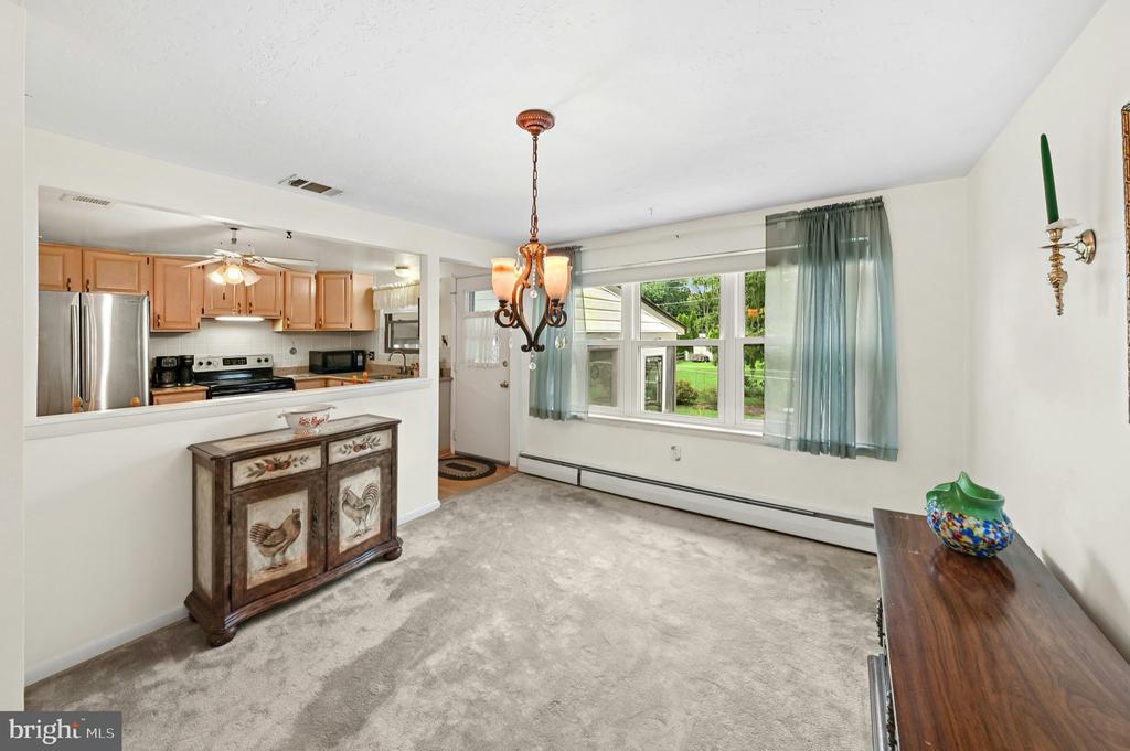 Dining room with a chandelier, large curtained window, and open connection to the kitchen.