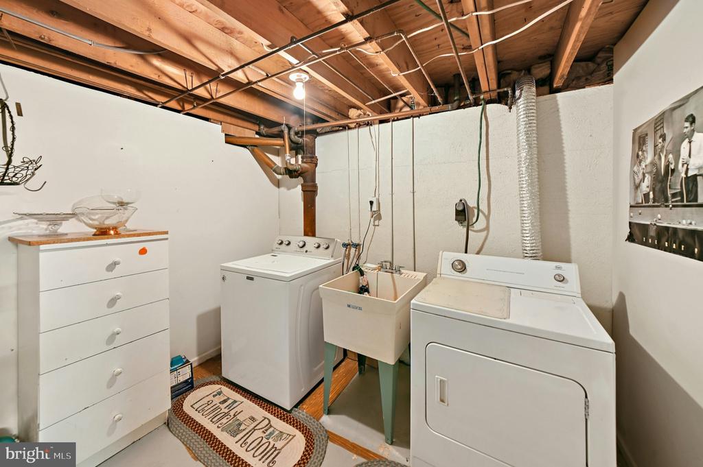 Basement laundry room with washer, dryer, utility sink, and exposed ceiling joists.