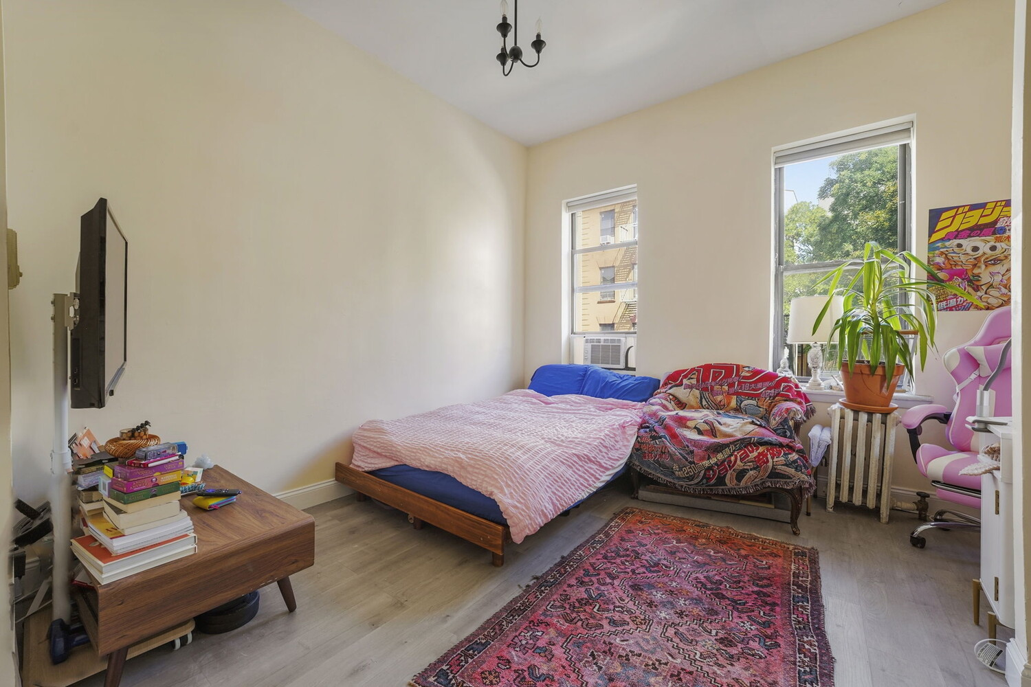 Furnished bedroom with colorful bedding, a pink rug, and windows overlooking trees.