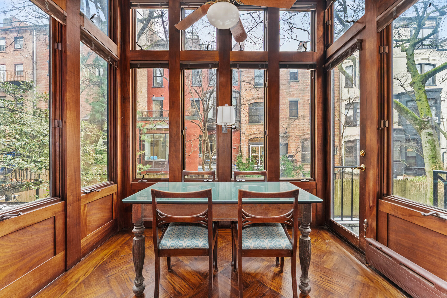 Dining area with a glass-top table and chairs in a wood-framed glass sunroom.