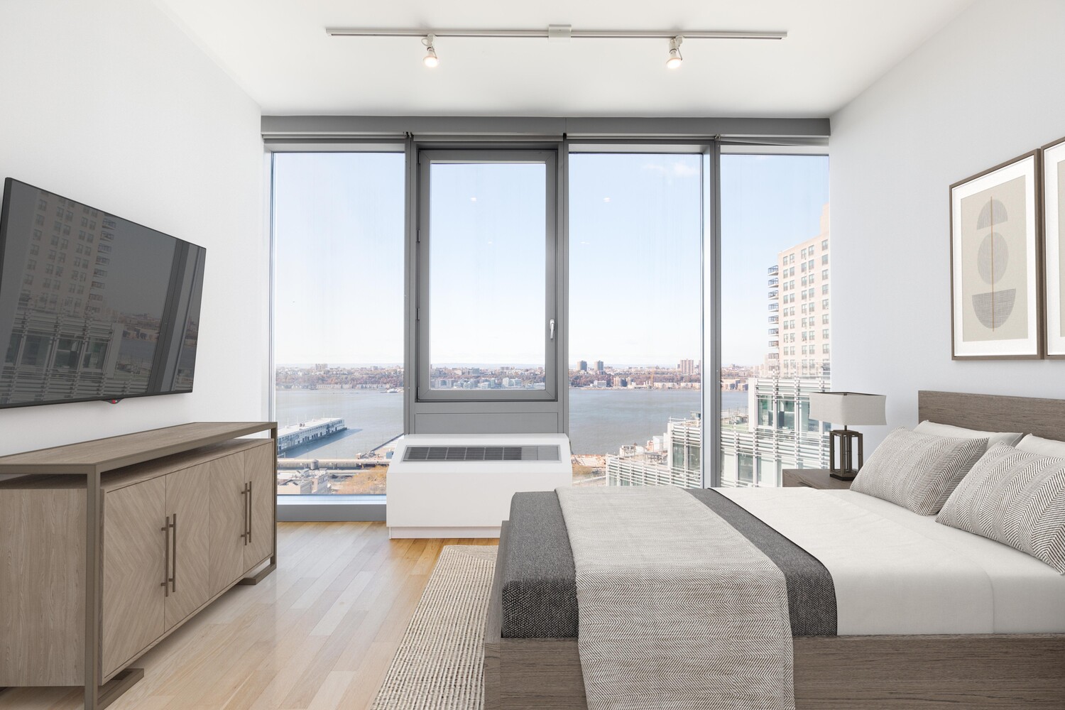 Bright bedroom with floor-to-ceiling windows overlooking a river and city skyline.