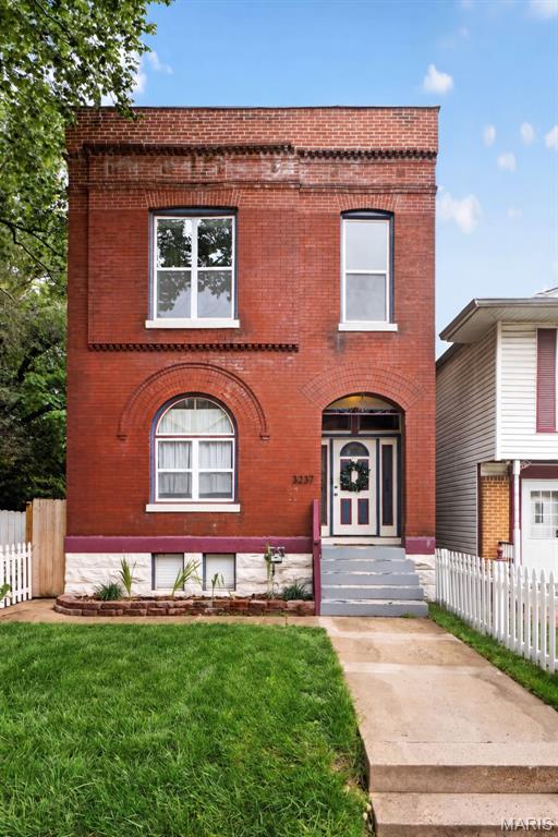 Two-story red-brick home with arched windows, gray front steps, a green lawn, and white picket fence.