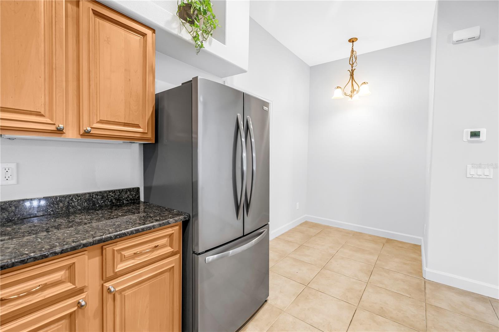 Kitchen with wood cabinets, granite counters, and a stainless steel refrigerator beside an empty dining area.