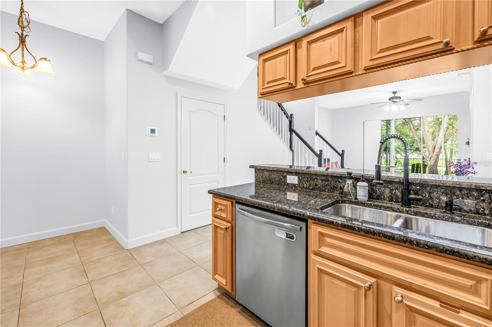 Kitchen with honey-colored cabinets, dark granite counters, and a double stainless-steel sink.