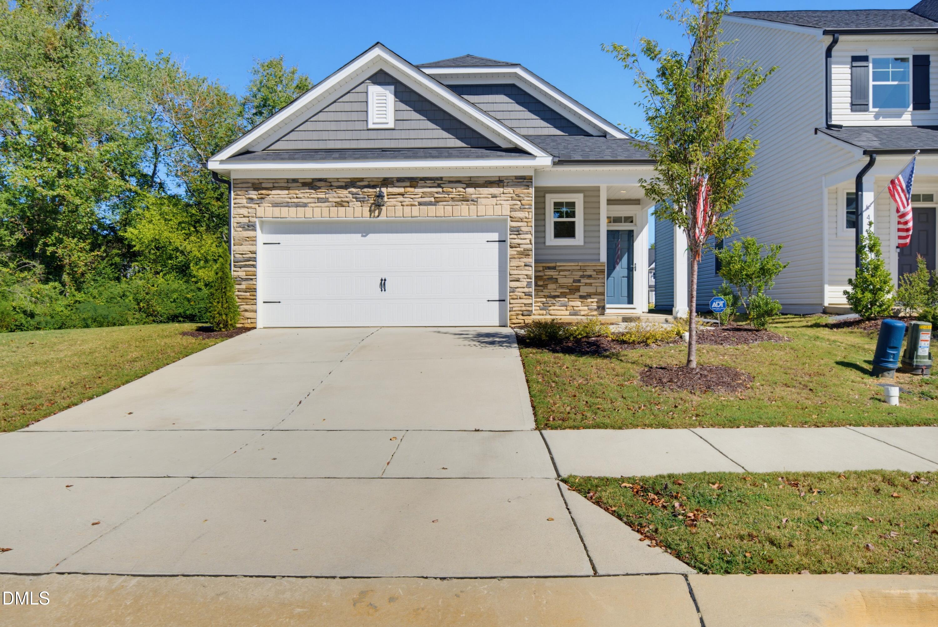 Gray home with stone-fronted garage, blue entry door, and wide concrete driveway.