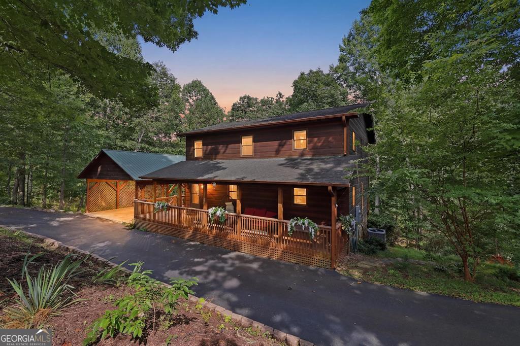 Two-story wood home with a covered porch and carport, surrounded by trees at dusk.