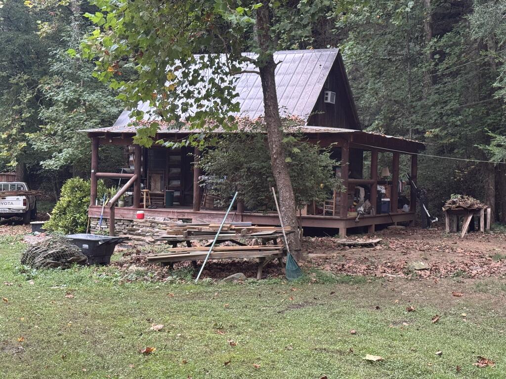 Rustic cabin with a metal roof and covered porch in a wooded clearing.