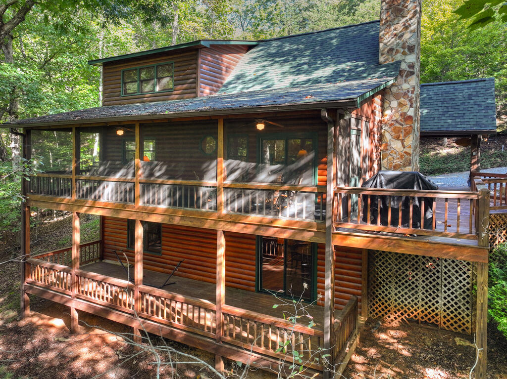 Log cabin among trees with two levels of wooden decks and a tall stone chimney.