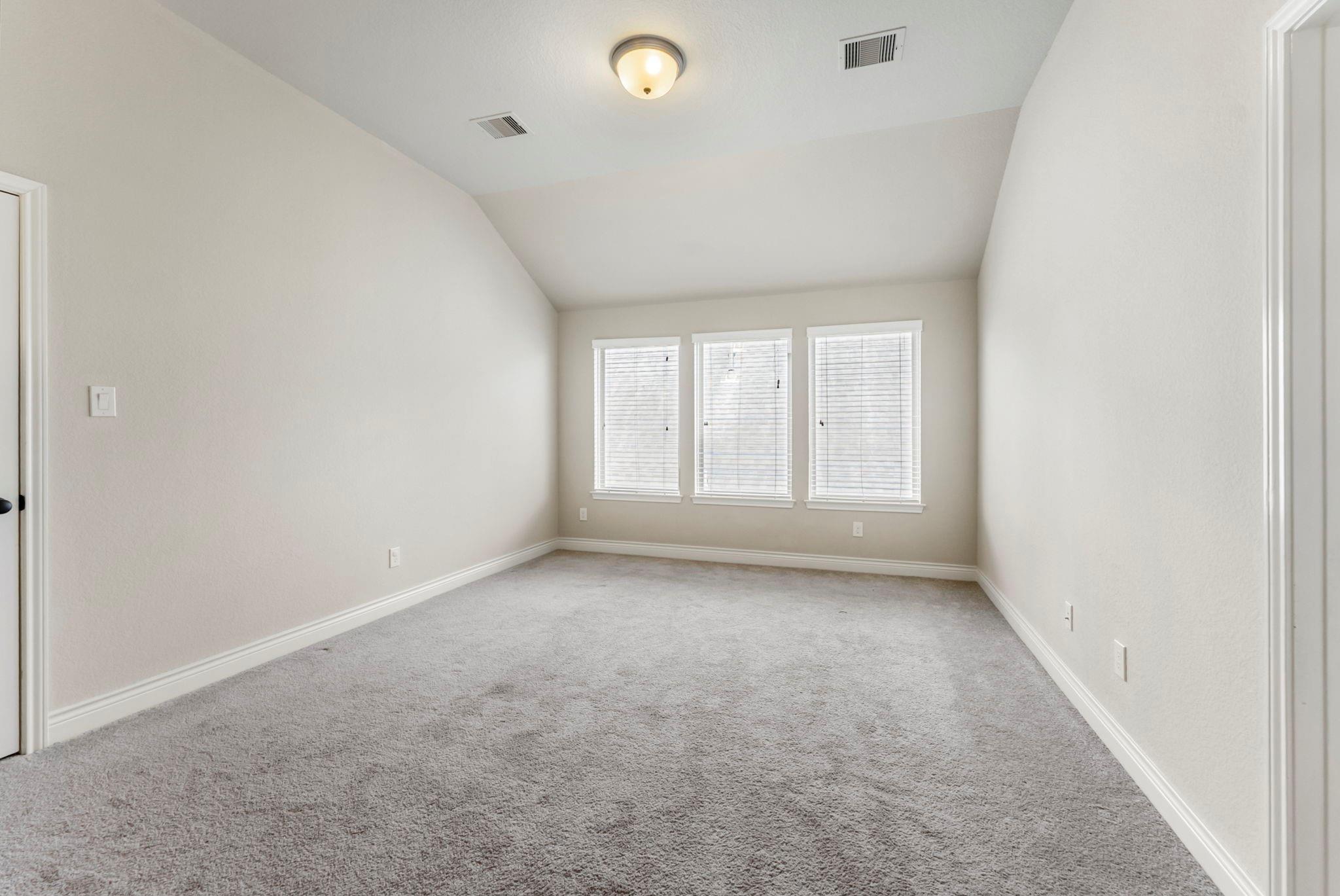 Empty carpeted room with a high angled ceiling and three windows with blinds.