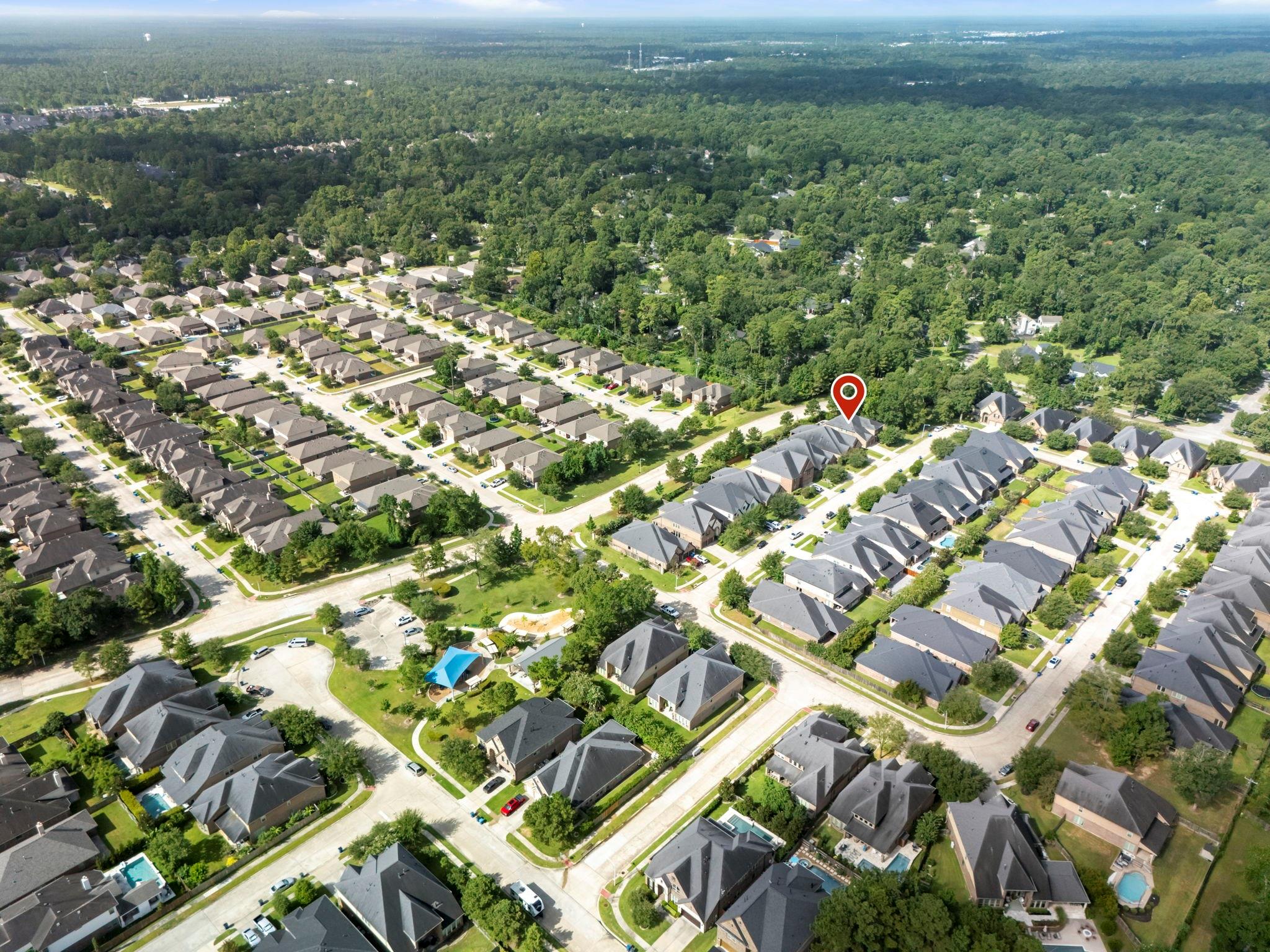 Aerial view of the marked house in a tree-lined neighborhood beside dense woodland.