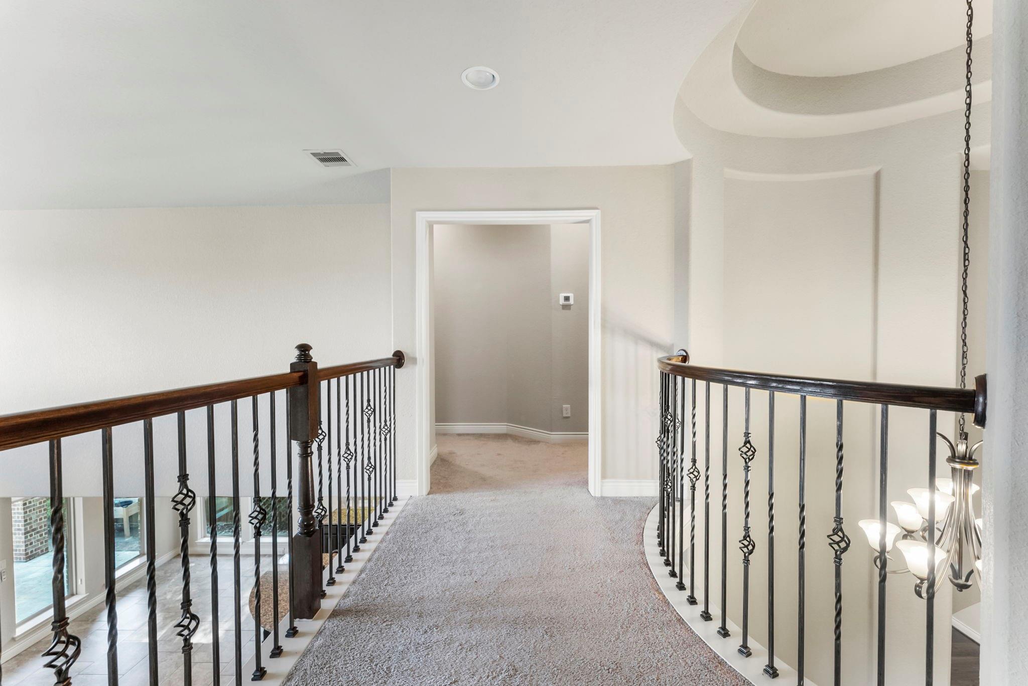 Upstairs landing with wrought-iron railings, beige carpet, and a hanging chandelier.