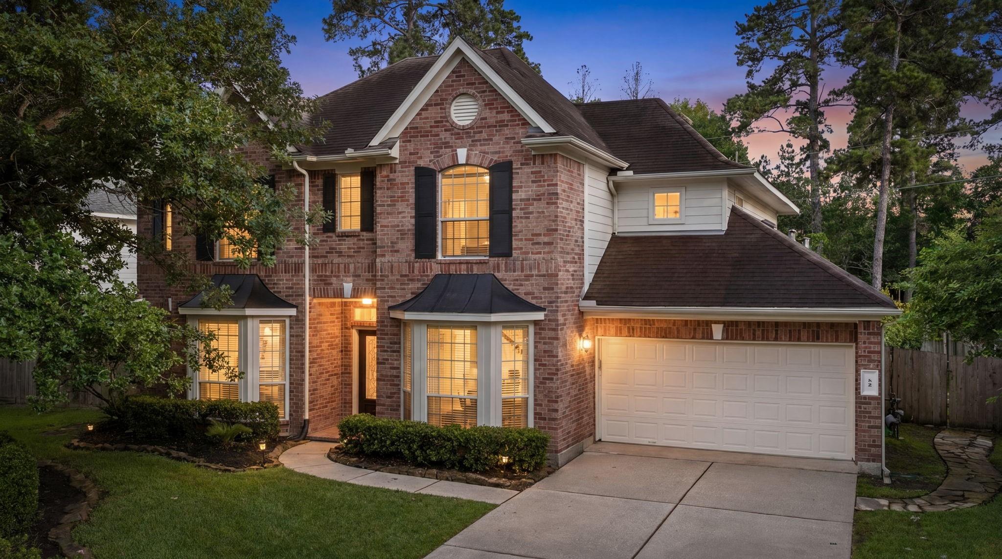 Two-story brick house with a double garage and warmly lit windows at dusk.
