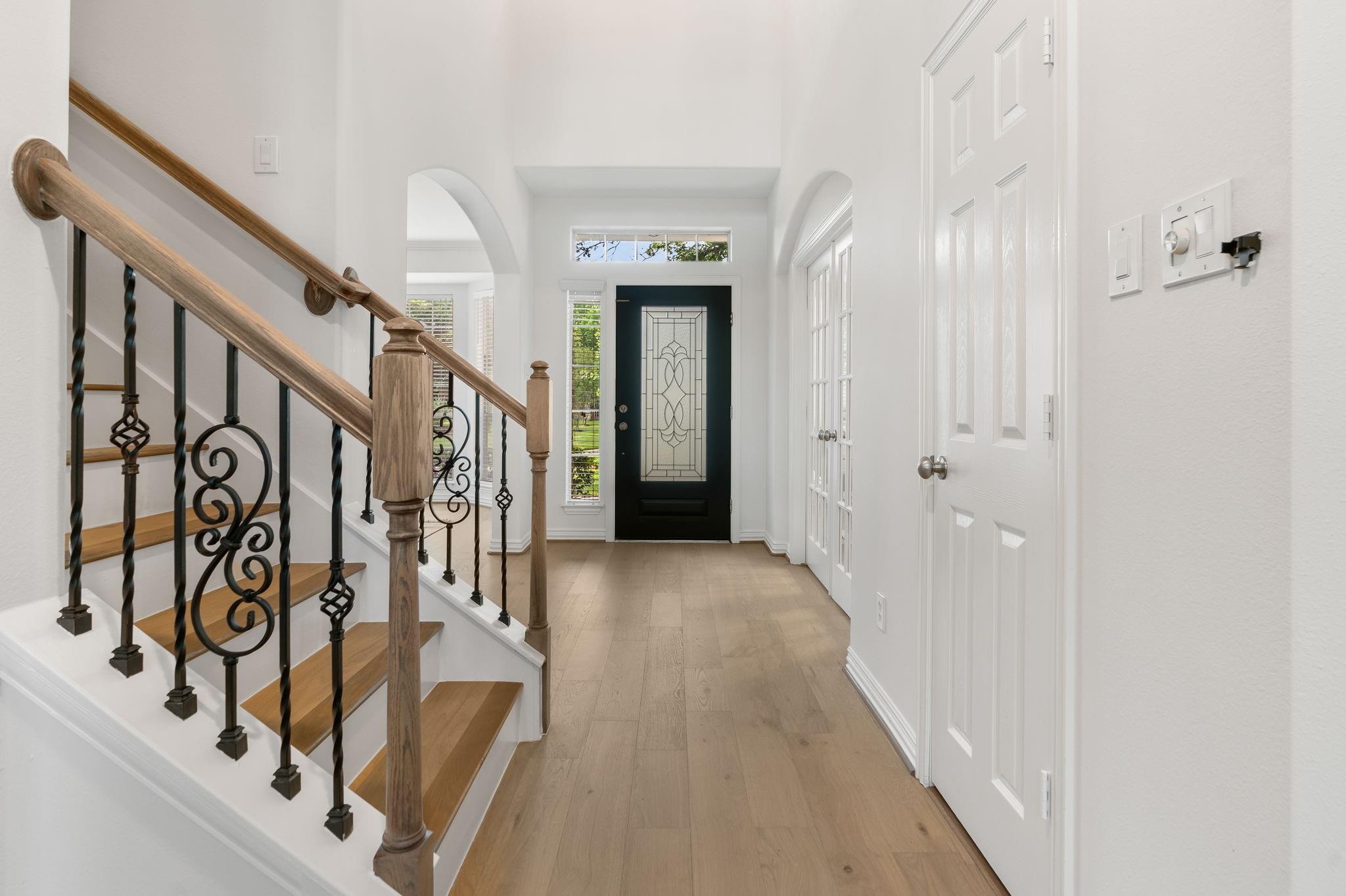 Entry hall with a wood-and-iron staircase and black front door with patterned glass.