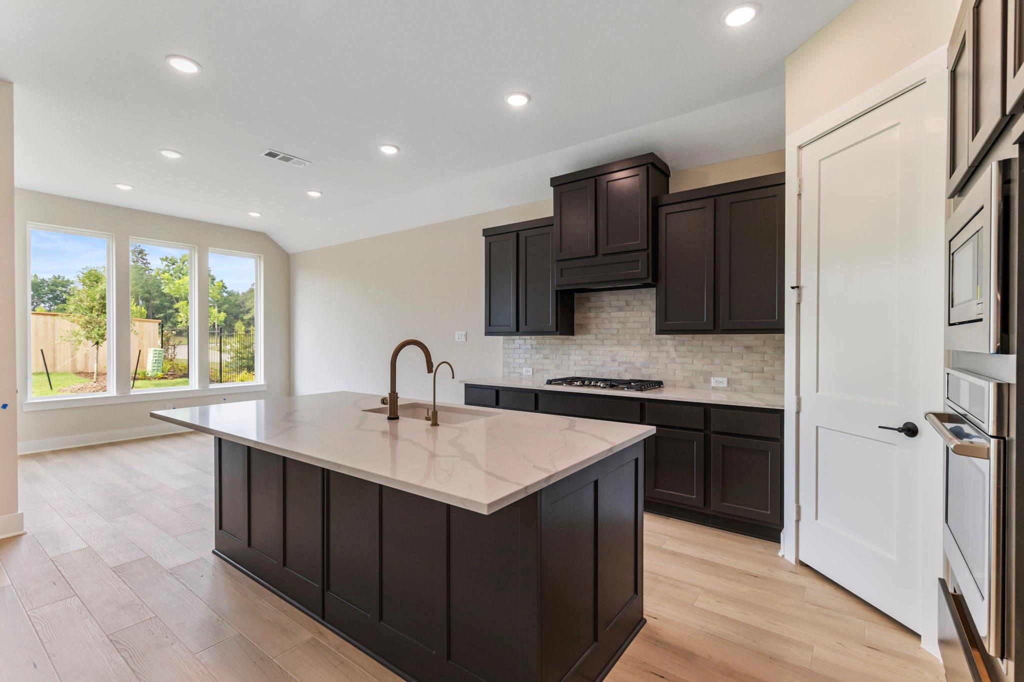 Kitchen with a large white island, dark cabinets, and three windows overlooking the yard.