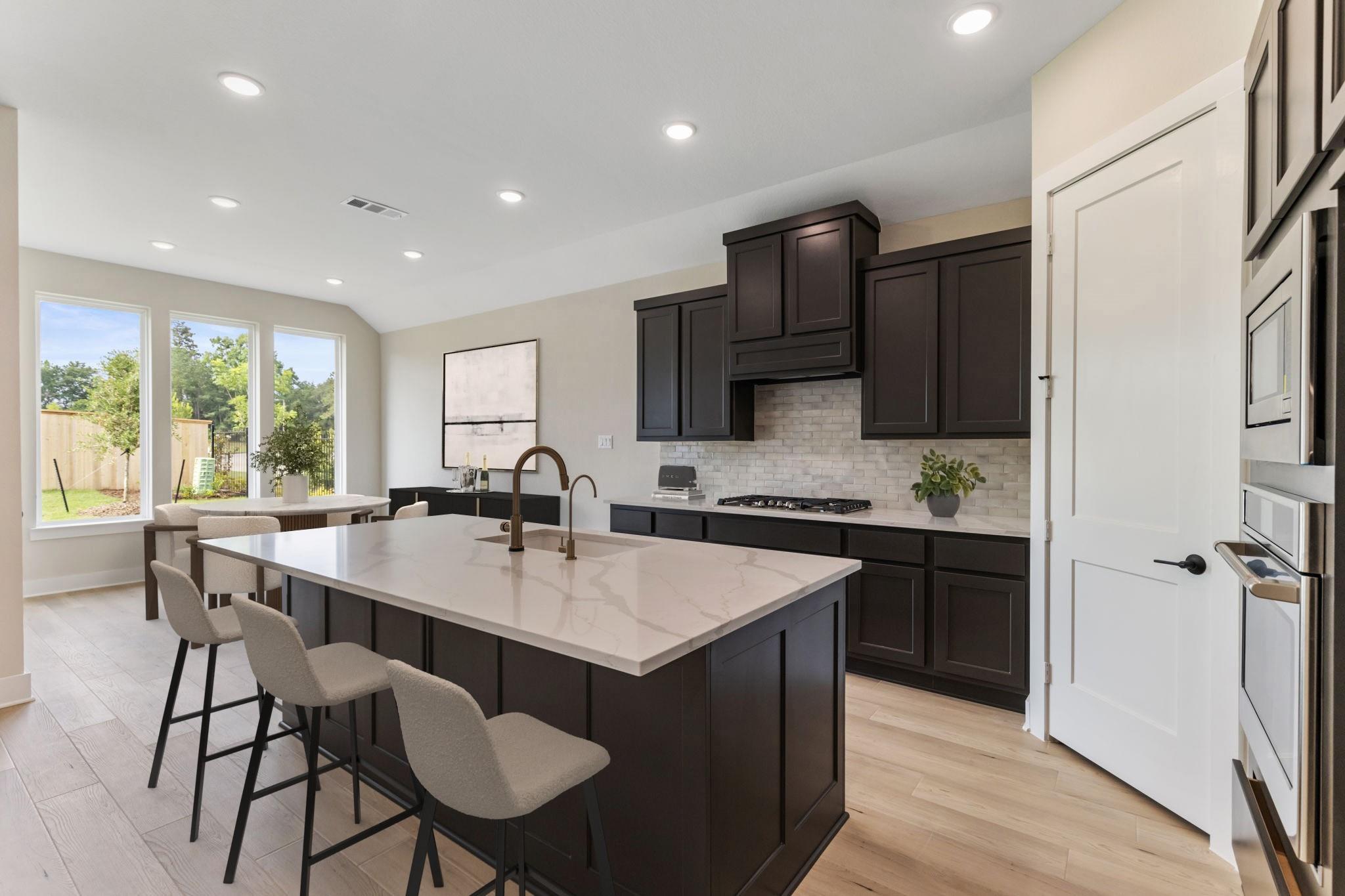 Kitchen with a large quartz island, dark cabinetry, gas cooktop, and built-in double ovens.