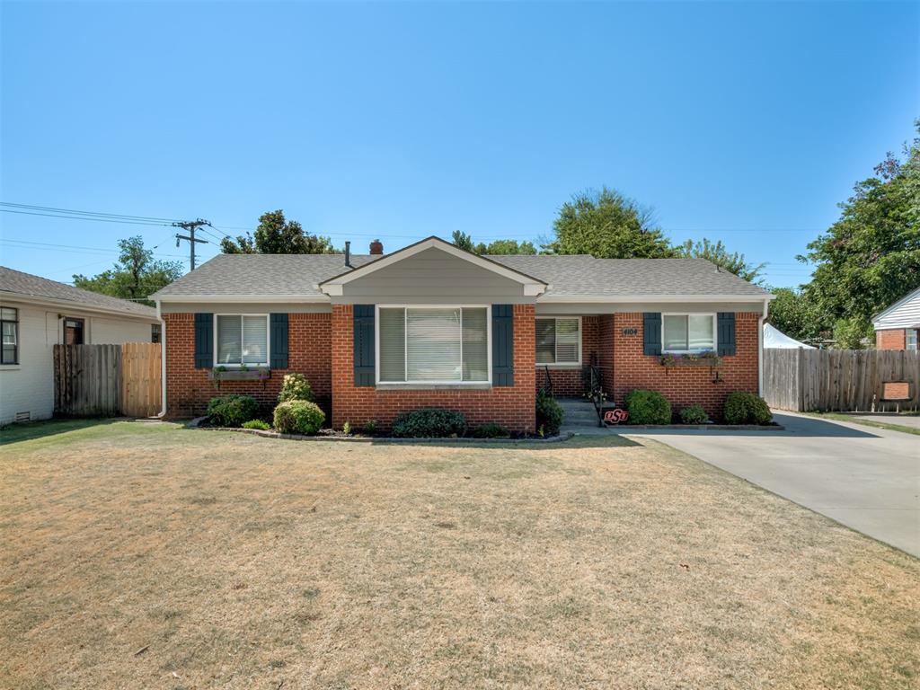 Single-story brick house with blue shutters, a landscaped front garden, and a concrete driveway.