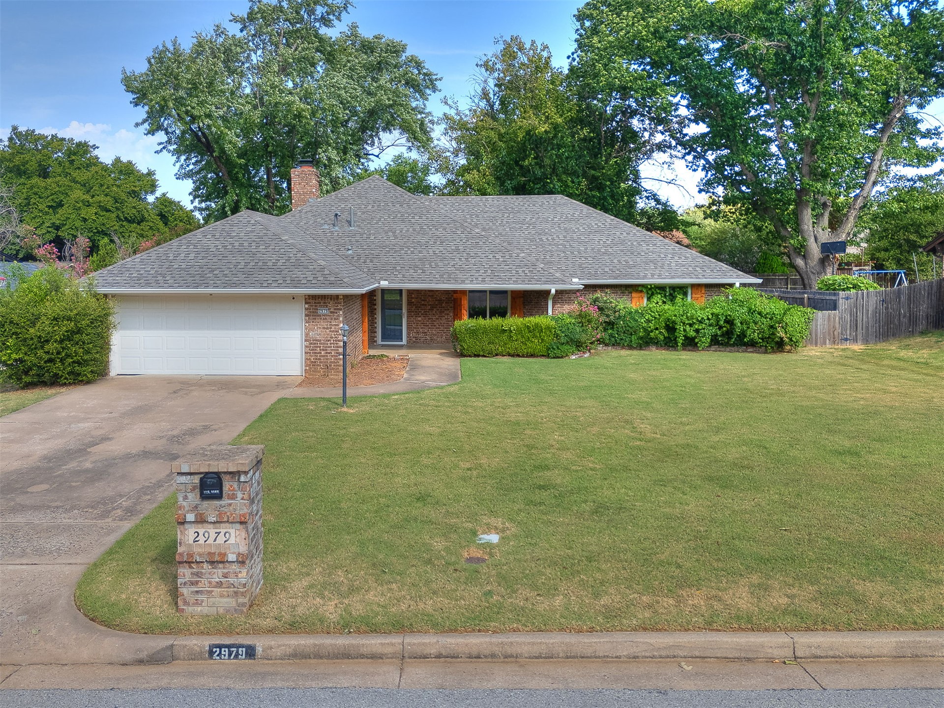 Brick ranch home with a white double garage, broad lawn, and mature trees.
