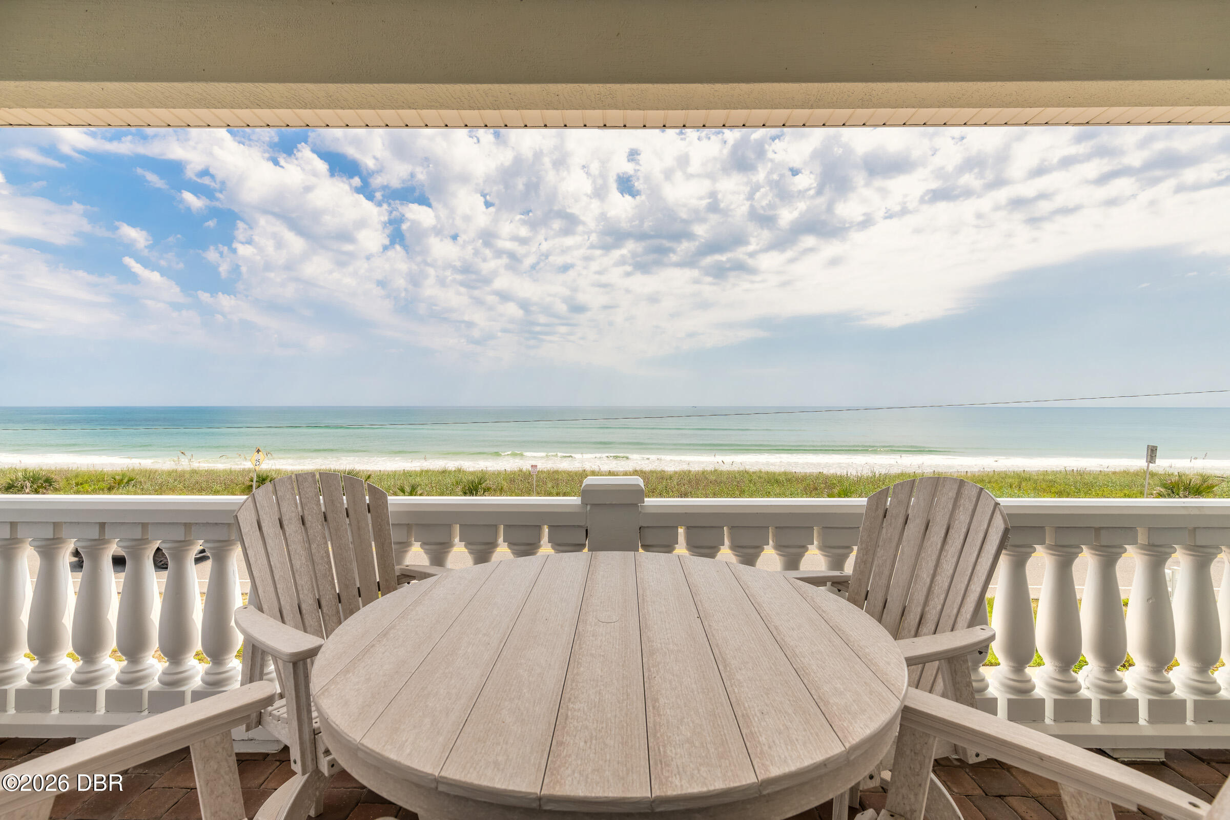 Covered oceanfront deck with a round wooden table and chairs overlooking the beach and ocean.