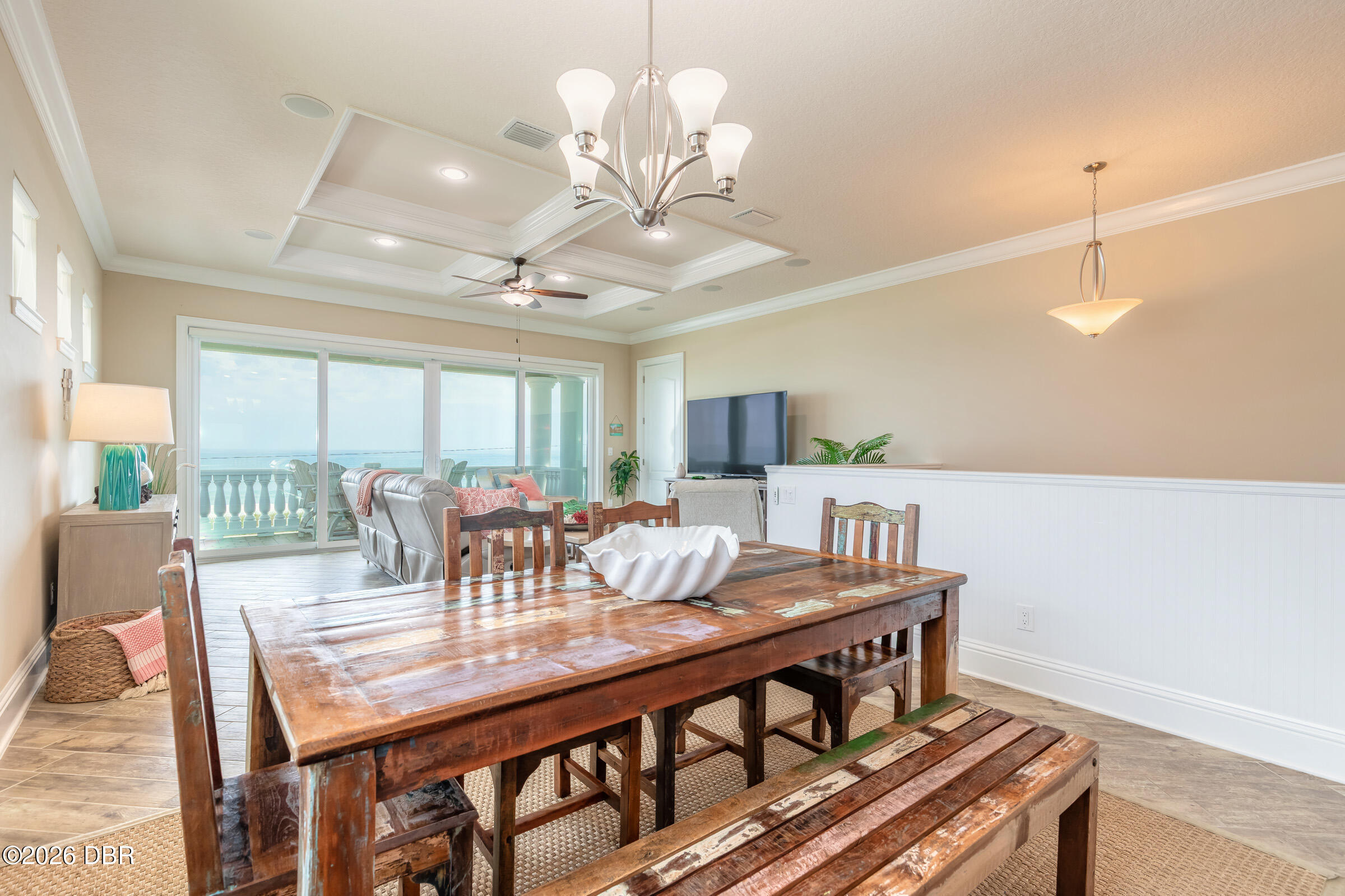 Dining room with a rustic wood table, adjoining living area, and ocean view through sliding glass doors.