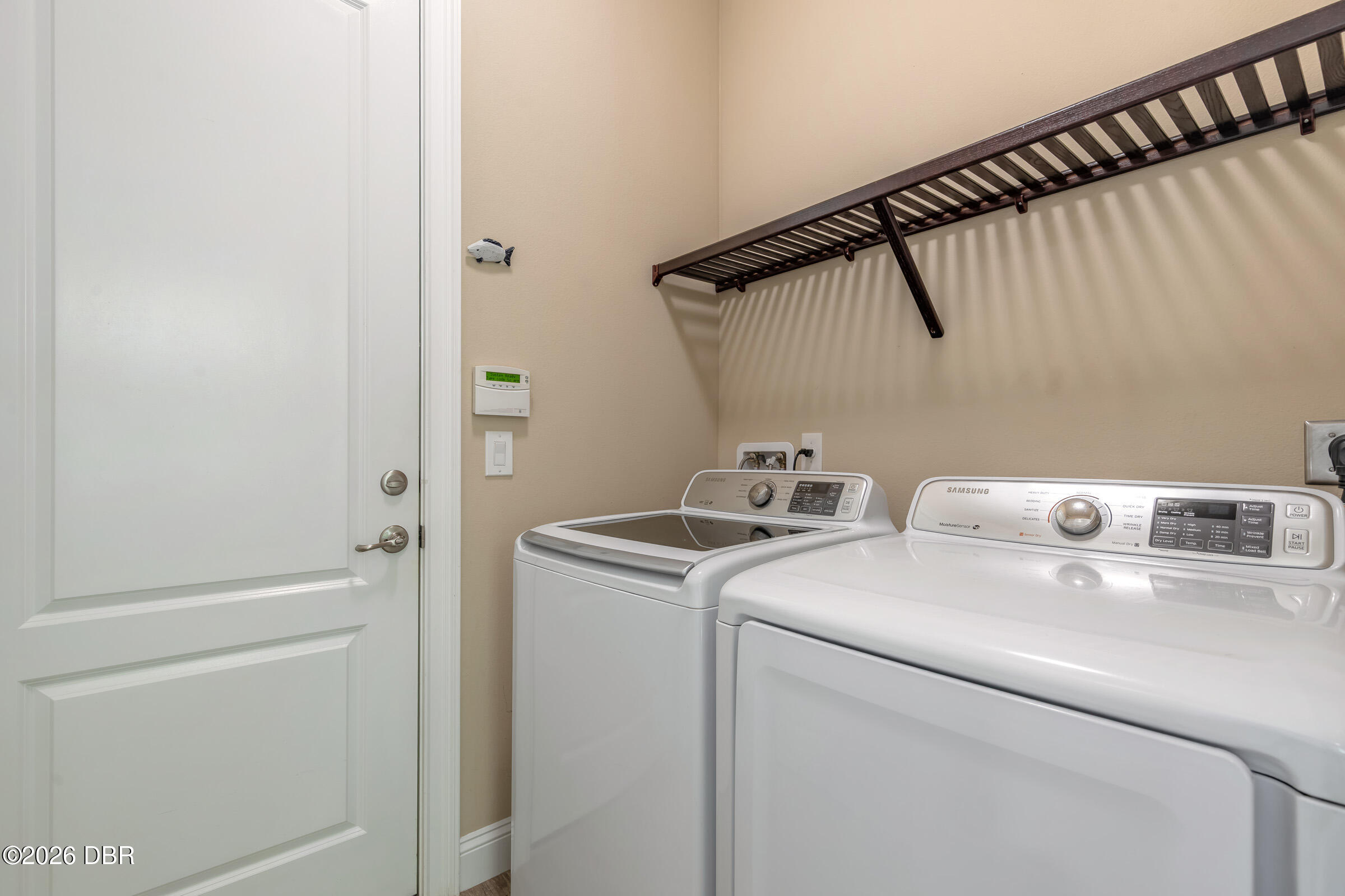 Laundry room with matching white washer and dryer beneath a dark open wall shelf.