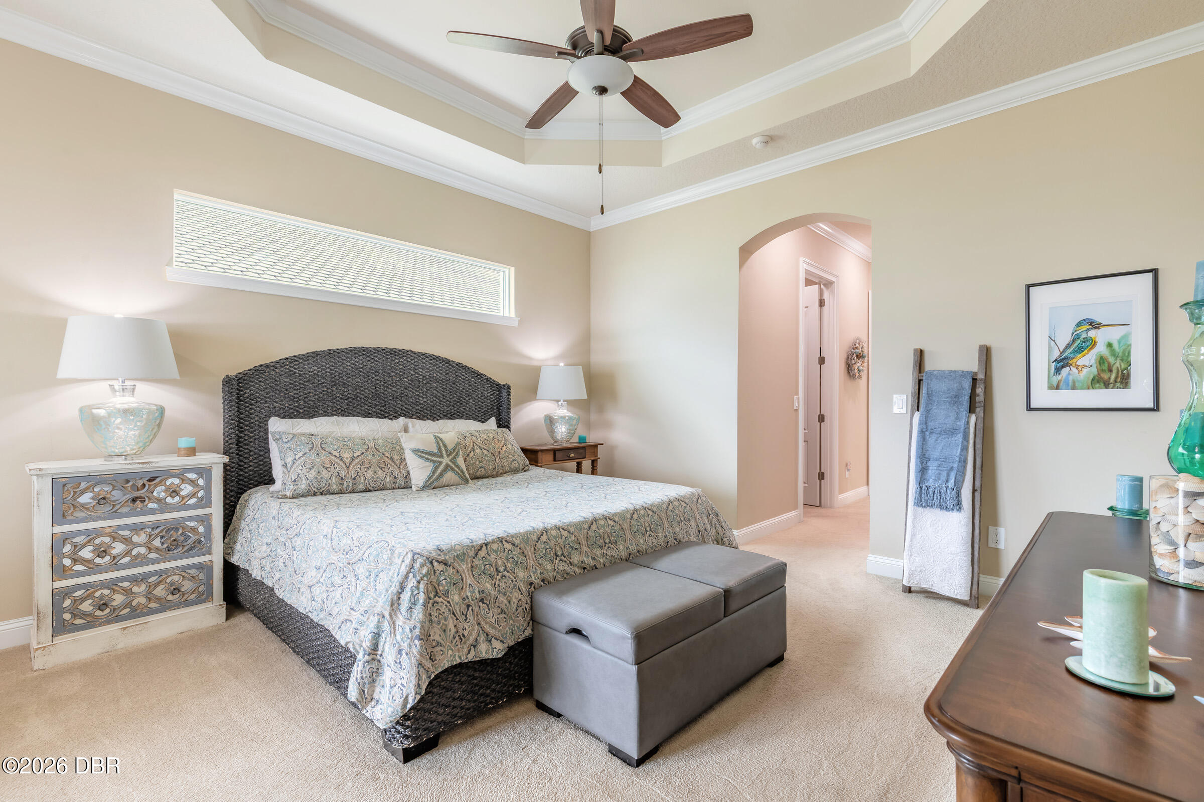 Bedroom with patterned bedding, a woven bed frame, and a tray ceiling with a ceiling fan.