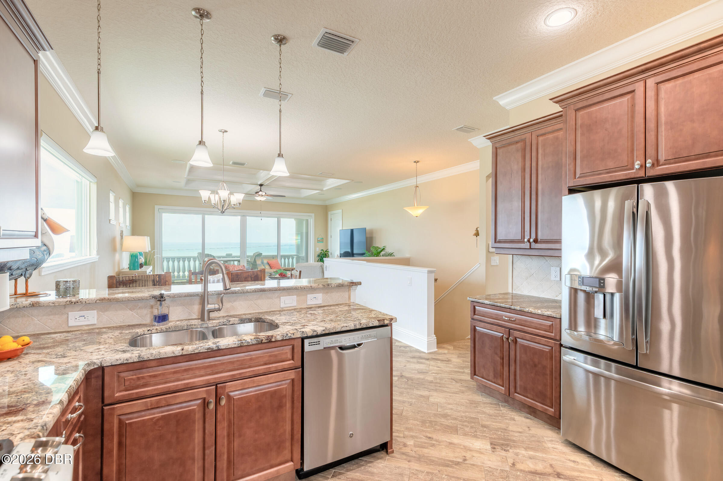 Kitchen with reddish-brown cabinets and granite counters, open to an ocean-view living area.