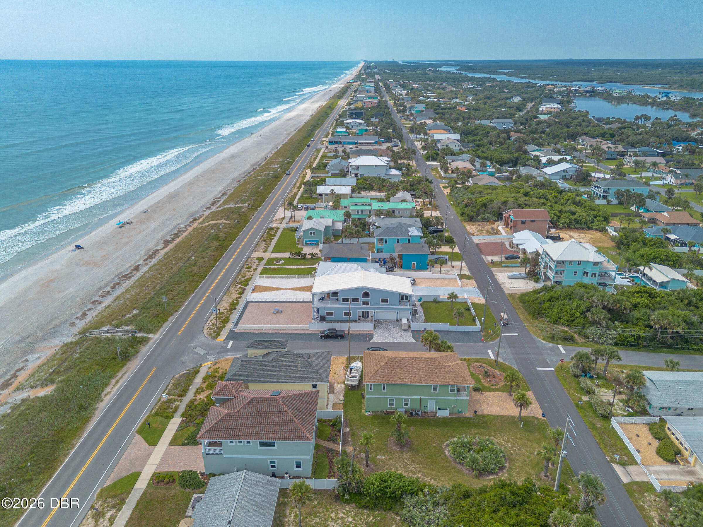 Aerial view of a coastal home beside the beach, ocean, and beachfront road.