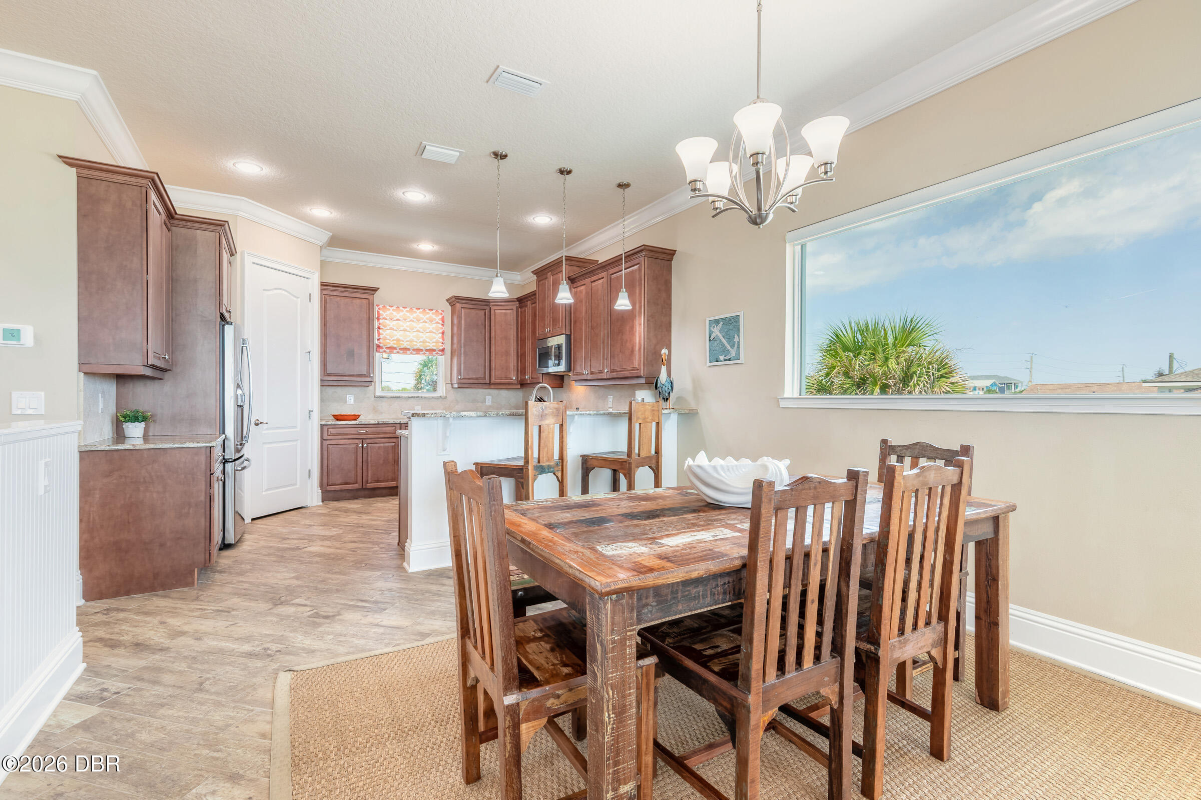 Open-plan kitchen and dining area with reddish-brown cabinets, a white breakfast bar, and rustic wooden furniture.