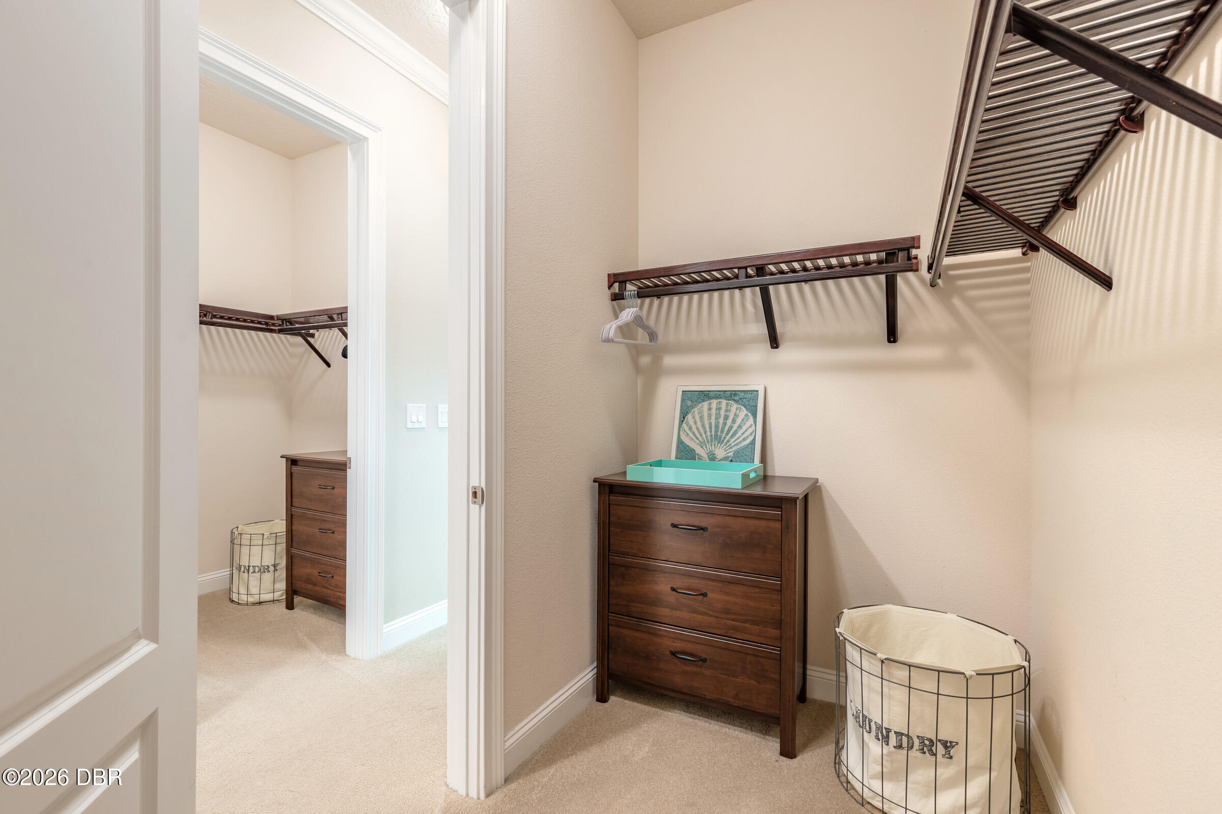 Walk-in closet with dark wood shelving, a matching dresser, wire laundry hampers, and shell artwork.
